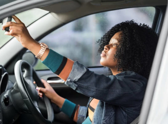 Shot of a mature african woman sitting in a car driving seat and adjusting rear view mirror